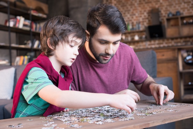 side view of focused father and son playing with puzzles at home