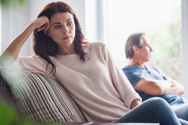 A couple of adults are quarreling while sitting on couch at home