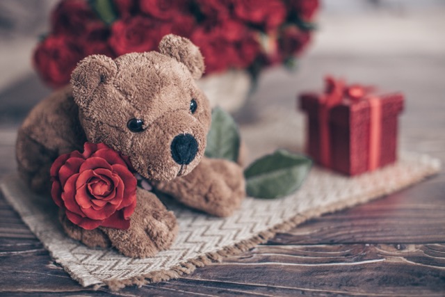 A Teddy bear a red rose and gift box on a mat.