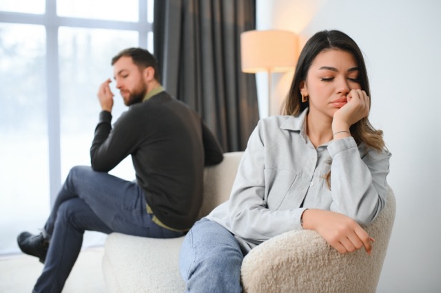 Beautiful couple is sitting back to back on the couch while having a quarrel.