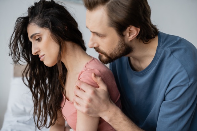 Caring bearded man calming down displeased girlfriend in bedroom at home