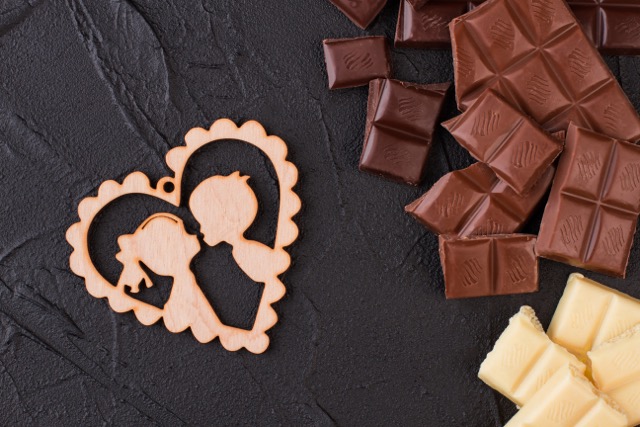 Chunk of chocolate and wooden heart on black background. Chocolate pieces and plywood heart. Happy Valentines Day.