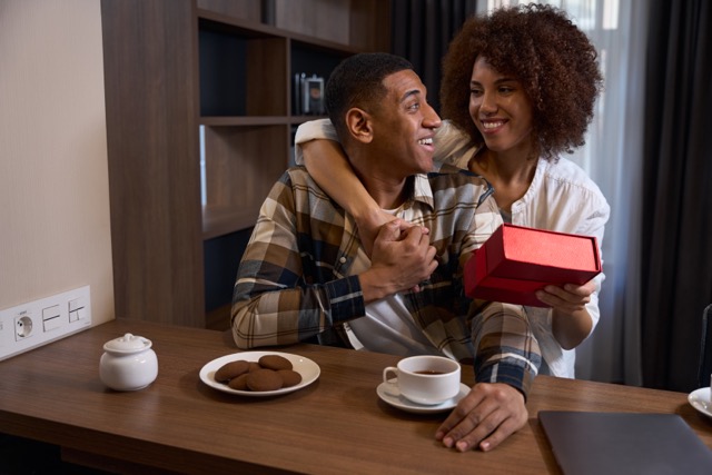 Cute multiracial wife giving chocolate box to husband at hotel breakfast; it's a chocolate day