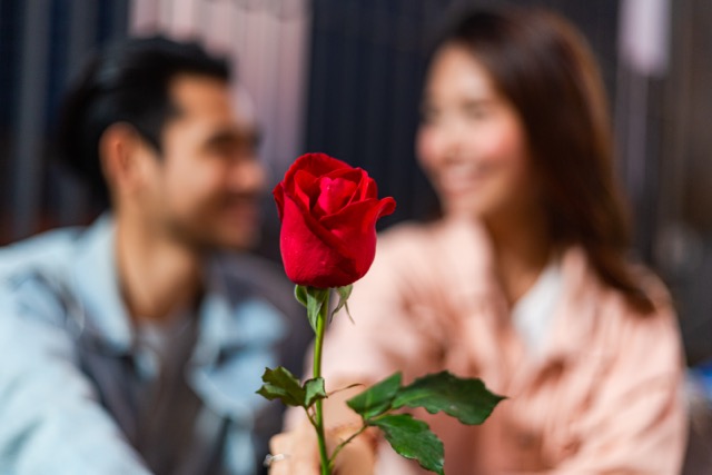 Rose Day Gift Ideas Beyond Flowers:Focus on flower with happy smile Asian couple holding rose, man and woman having romantic dating on Valentine's, Anniversary or birthday, Marriage proposal and engagement with love together concept
