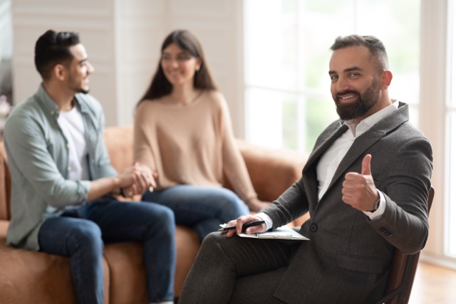 Successful marriage coaching. Professional male marriage therapist gesturing thumb up while working with a young marriage couple at office. 