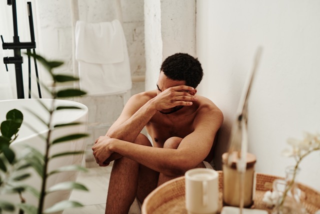 Young man sitting on floor in bathroom and rubbing his eyes from tears, he crying alone