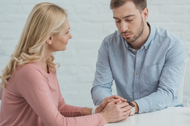 Wife and Hasbend holding hands while sitting at table. 