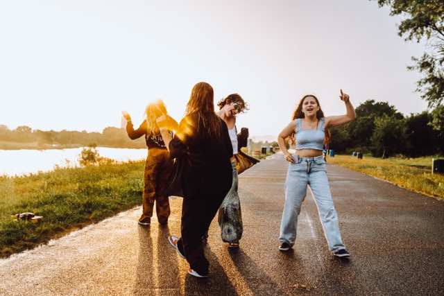 party young happy girls in nature. company young women, teenage girls, smiling, with hair wet from rain, having fun, taking selfies and dancing in nature by river, in rays of setting sun, glare lens.