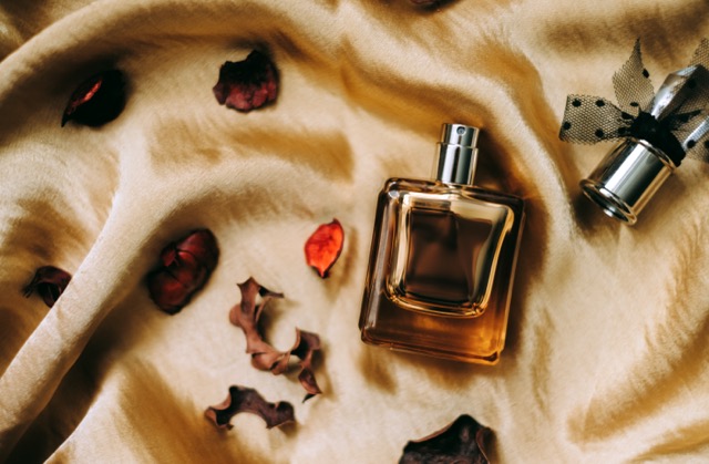 Perfume bottle on golden satin fabric with dried flower petals, flat lay, warm light.