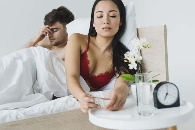 selective focus of pretty asian woman taking birth control pills from bedside table while lying near