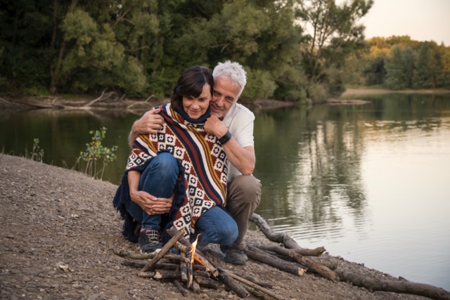 Senior happy couple at campfire at a lake.