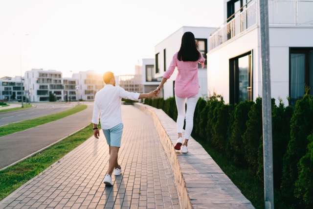 Back view of faceless girlfriend in casual clothes walking on stone curb and holding hands with boyfriend during date on city street on weekend