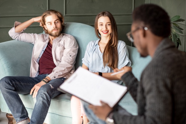 A marriage couple visits a Marriagr therapist sitting on the comfortable couch during therapist  session in the green office.