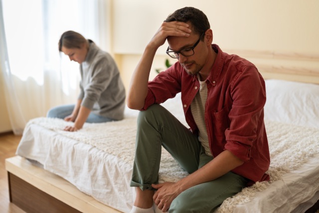 Young unhappy European family couple sitting separately on bed at home, thinking of breakup, having problems in relationship. 