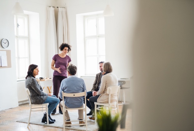 A young woman standing and talking to other people during life group therapy.