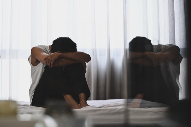 Depressed husband sitting in the dark bedroom with a low light environment. Mental health, depression, sad emotional, mental illness.