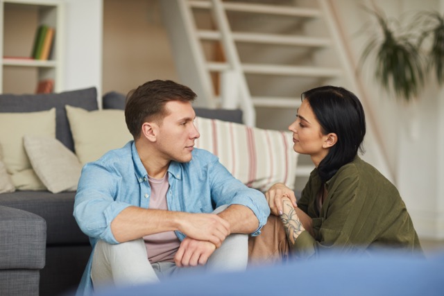 Marriage couple talking their problem to each other sincerely on floor in cozy home interior.